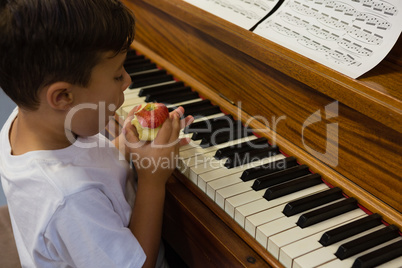 High angle view of boy eating apple while sitting by piano