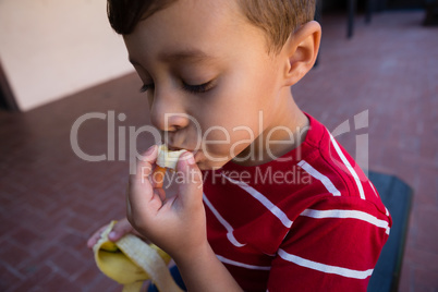 Close up of boy eating banana while sitting on chair