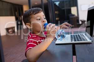 Boy drinking water while using laptop at table