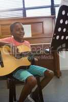 Happy boy playing guitar while sitting in classroom