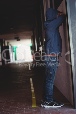 Side view of sad boy leaning on wall in corridor