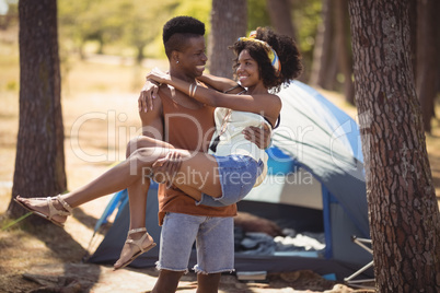 Happy man carrying woman while standing against tent