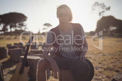 Portrait of young man sitting by guitar on tree stump