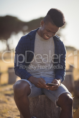 Smiling man using smart phone while sitting on tree stump