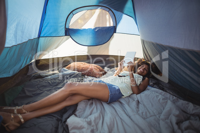 Happy woman using digital tablet while lying down in tent