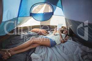Happy woman using digital tablet while lying down in tent