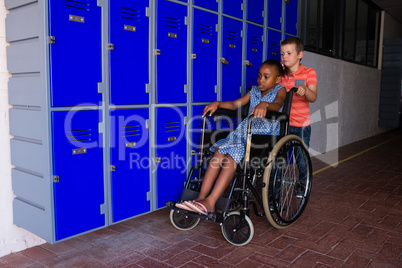 Boy with classmate sitting on wheelchair by lockers