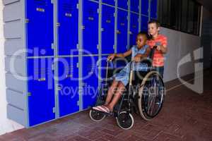 Boy with classmate sitting on wheelchair by lockers