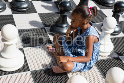 High angle view of thoughtful girl sitting by chess pieces