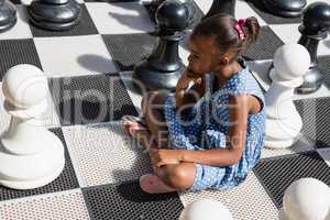 High angle view of thoughtful girl sitting by chess pieces