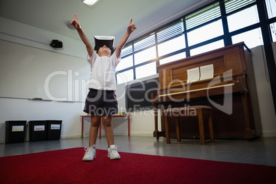Boy wearing virtual reality simulator raising hands while standing against piano