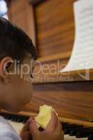 Close up of cute boy eating apple while sitting by piano