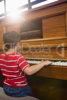 Rear view of boy playing piano in classroom