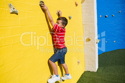 Portrait of smiling boy climbing yellow wall at playground