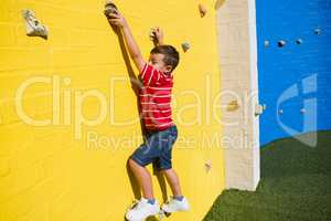 Portrait of smiling boy climbing yellow wall at playground