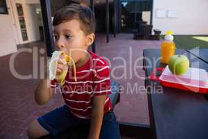 Boy looking away while eating banana at table