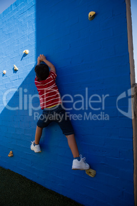Rear view of boy climbing blue wall at playground