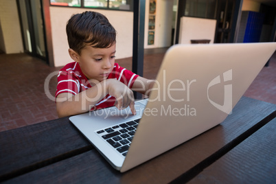 Cute boy working on digital laptop while sitting at table