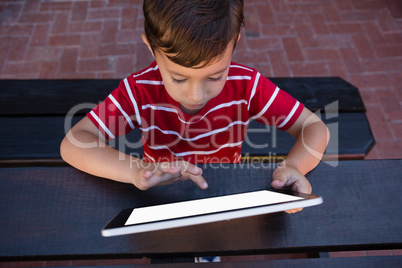 Boy touching digital tablet while sitting at table in school