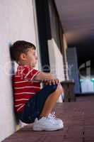 Side view of cute boy sitting by wall