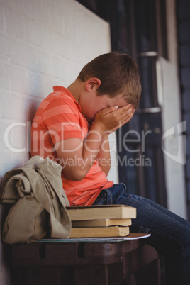 Unhappy boy covering face with hands while sitting on bench