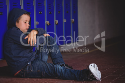 Sad boy sitting on pavement by lockers