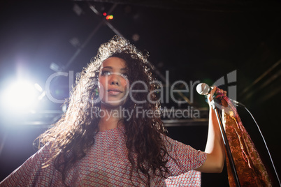 Thougthful young female singer holding mic at nightclub