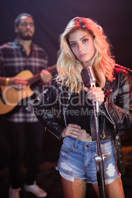 Portrait of young female singer with hand on hip and mic at nightclub