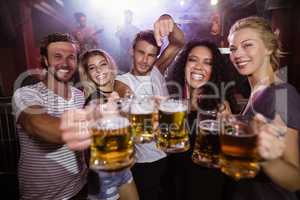 Portrait of happy friends holding beer mugs at nightclub