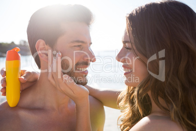 Happy woman applying sunscream on man face at beach