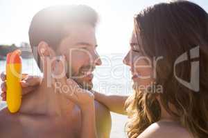 Happy woman applying sunscream on man face at beach