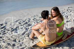 Couple sitting together on surfboard at beach