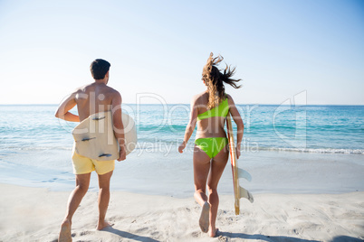 Rear view of couple running while holding surfboards at beach
