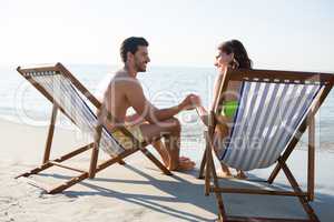 Happy couple holding hands while sitting on lounge chairs at beach
