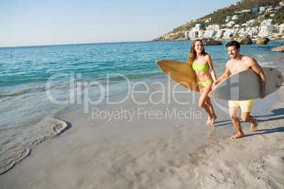 Happy couple running together while holding surfboards at beach