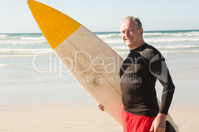 Portrait of senior man with surfboard standing at beach