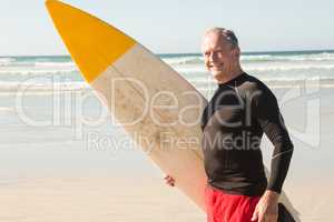 Portrait of senior man with surfboard standing at beach