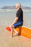 Side view of man sitting on surfboard at beach
