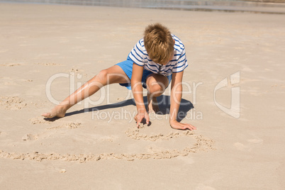 Boy playing with sand while crouching at beach