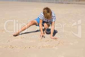 Boy playing with sand while crouching at beach