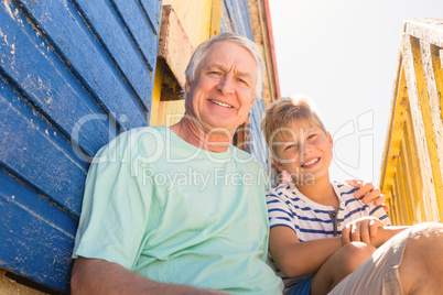 Portrait of smiling grandfather and boy sitting at beach hut