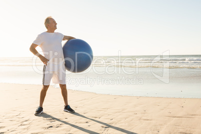 Senior man holding ball while standing at beach