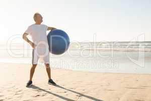 Senior man holding ball while standing at beach