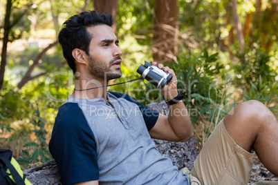 Man using binoculars while resting in the forest