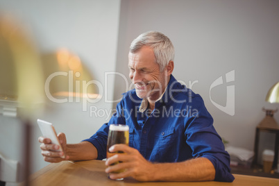Mature man using mobile phone while having beer