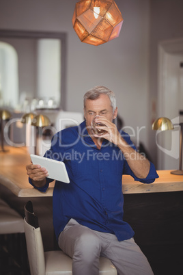 Mature man using digital tablet while having beer