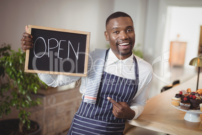 Smiling waiter showing chalkboard with open sign