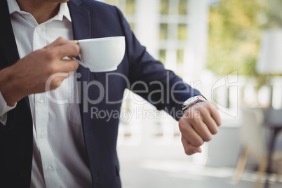 Mid section of businessman checking time while having coffee