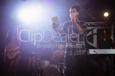 Male singer performing while holding digital tablet at nightclub