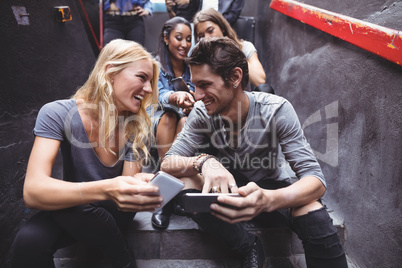 Cheerful friends using mobile phones on steps at nightclub